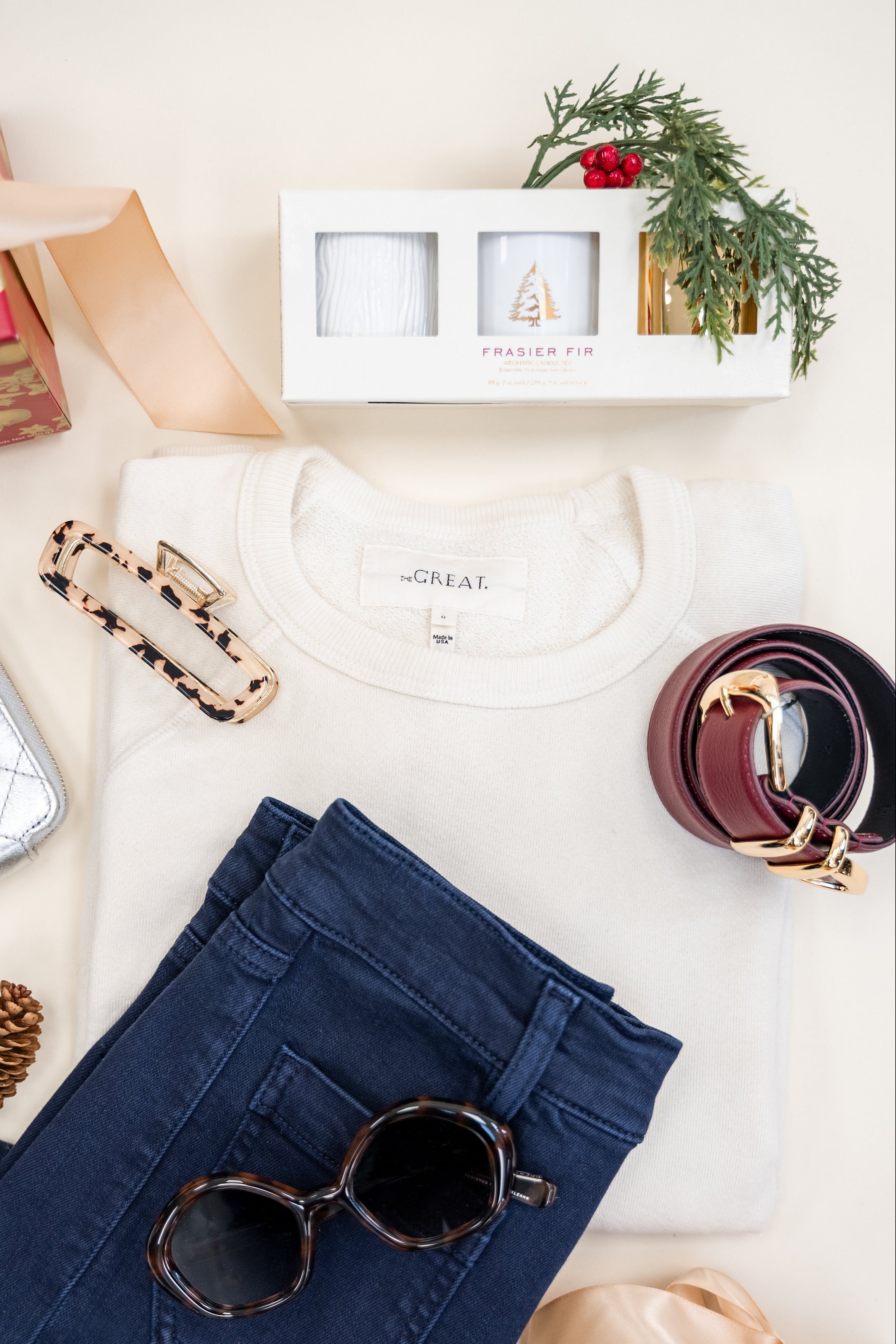 Flat lay of navy pants, sunglasses, a white shirt, and decorative items on a light surface.