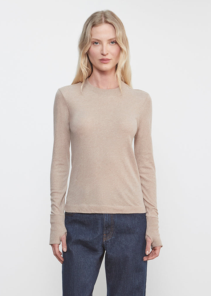 Woman wearing a beige long-sleeve top and dark blue jeans against a white background