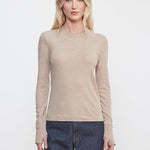 Woman wearing a beige long-sleeve top and dark blue jeans against a white background