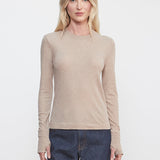 Woman wearing a beige long-sleeve top and dark blue jeans against a white background