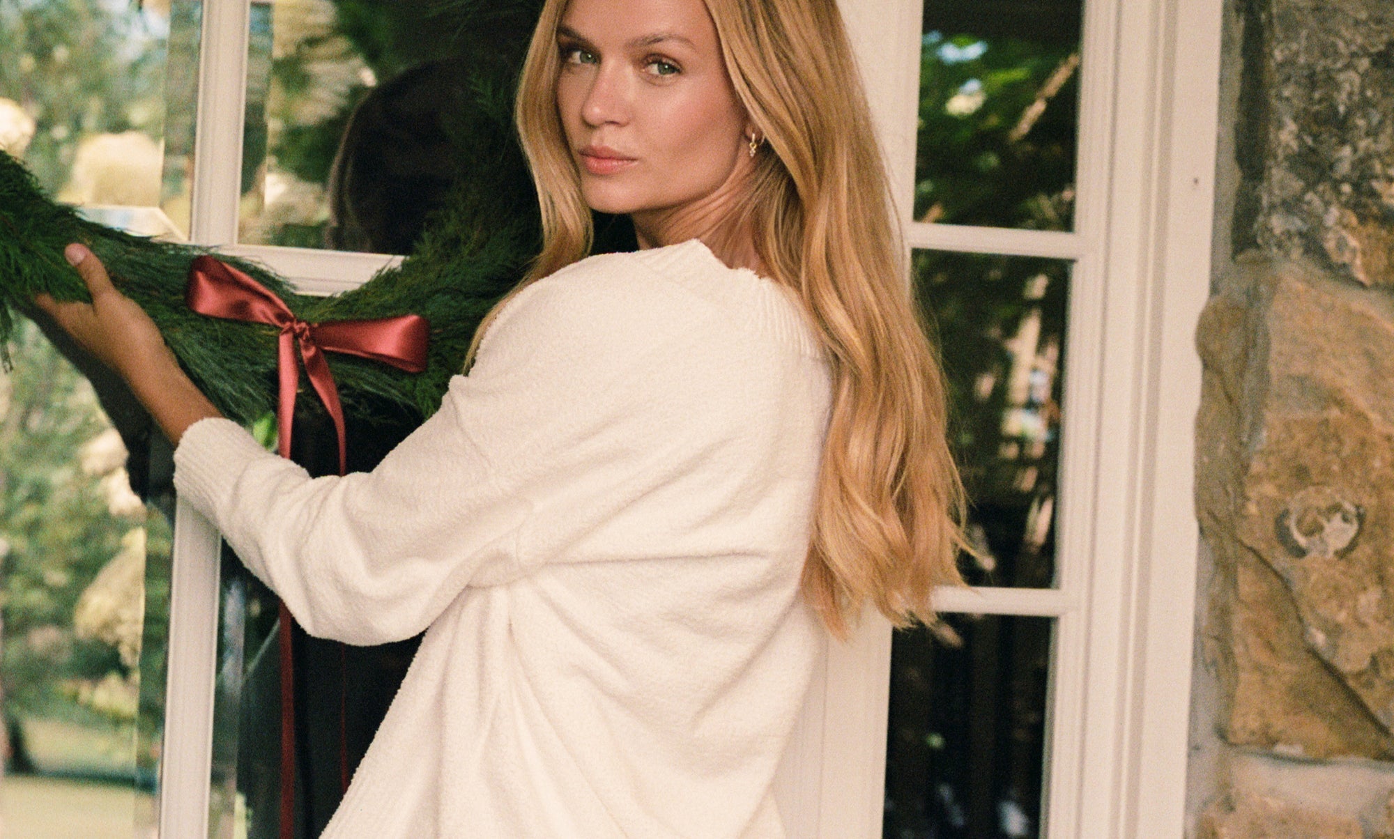 Woman holding a wreath with a red bow in front of a window.