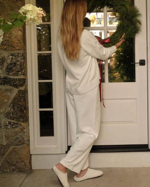 Woman in a white outfit sitting on a bench outside a house.