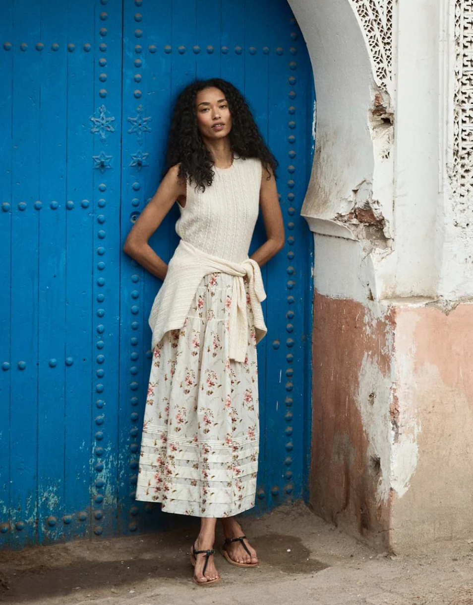 Woman in a white dress with floral pattern standing in front of a blue door.