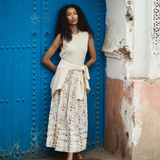 Woman in a white dress with floral pattern standing in front of a blue door.